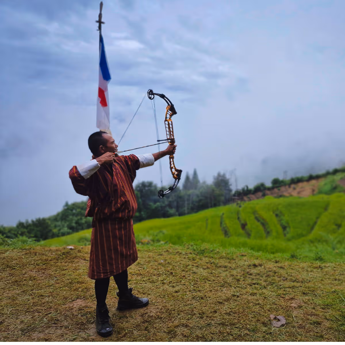 Bhutanese man aiming a modern bow on an archery ground.