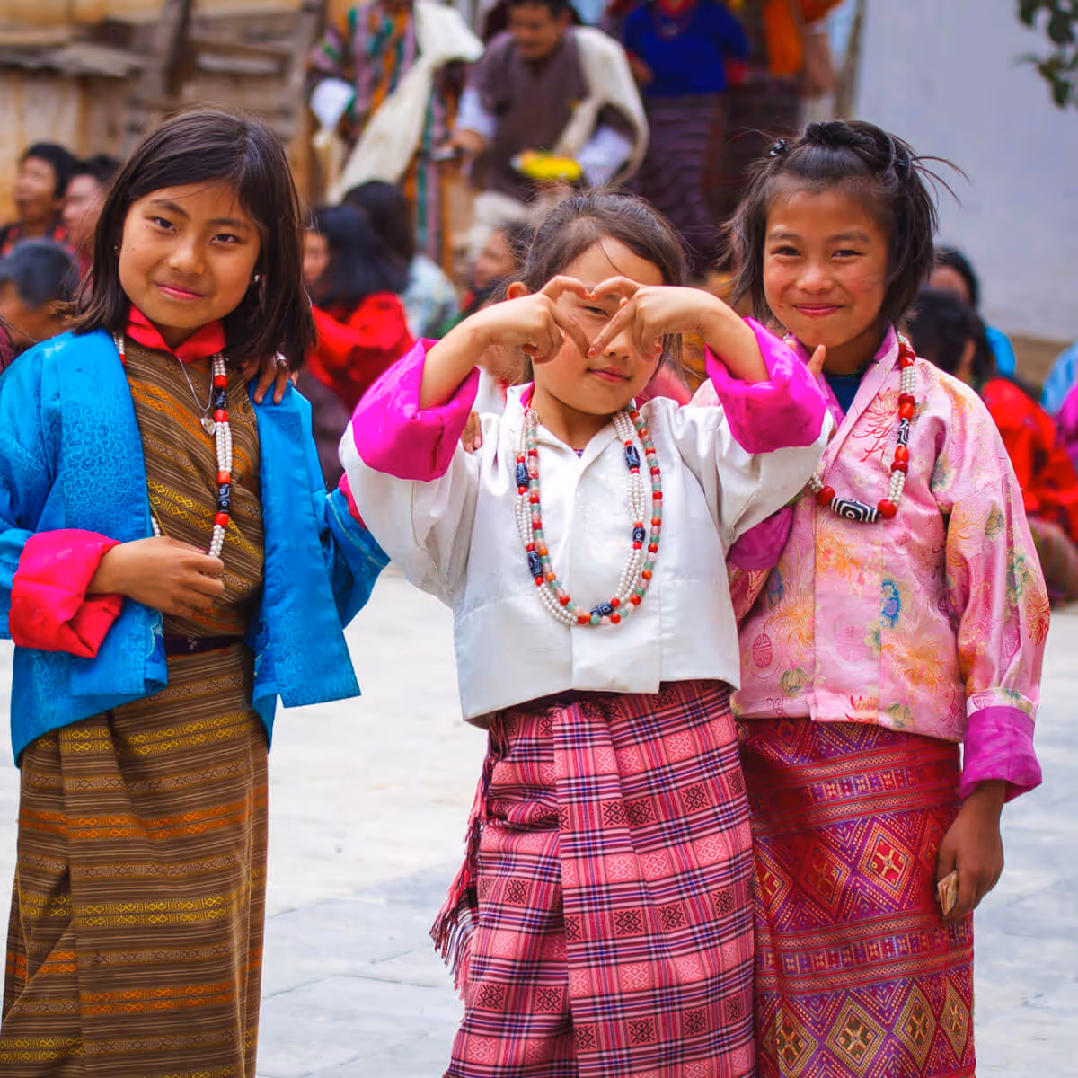 Three young girls in kira, one making a heart shape with her hands at a festival.