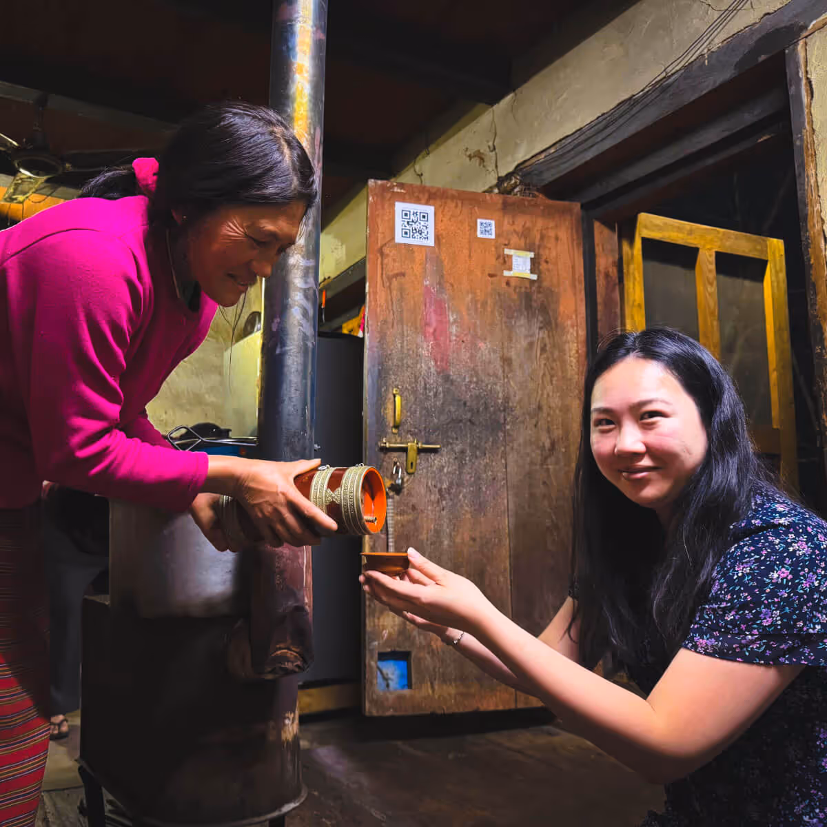 Guest receiving homemade wine in a Bhutanese farmhouse.