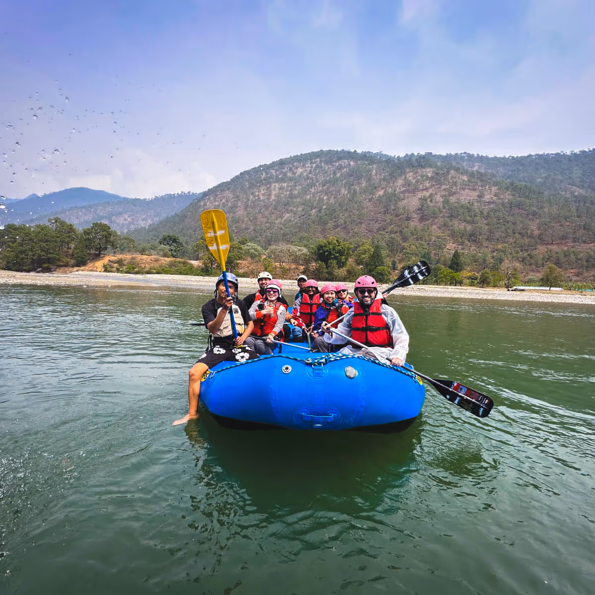 Group enjoying rafting adventure on a river in Bhutan, surrounded by forested hills.