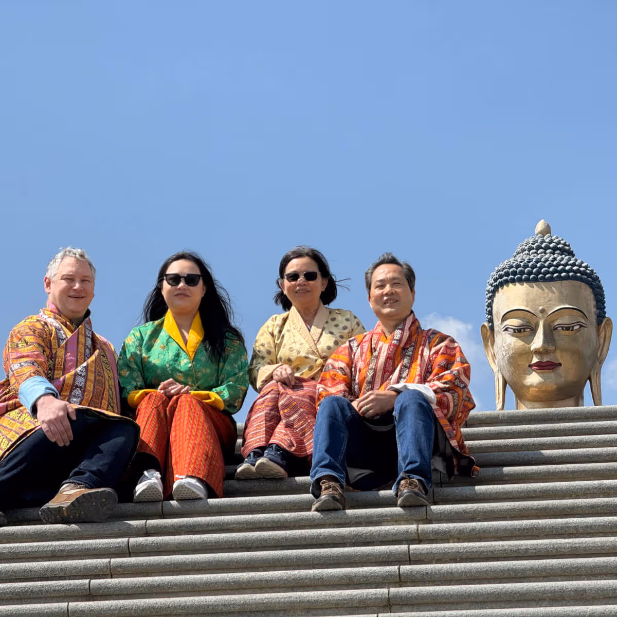 Travelers in traditional attire sitting near Buddha Dordenma statue in Thimphu, Bhutan.