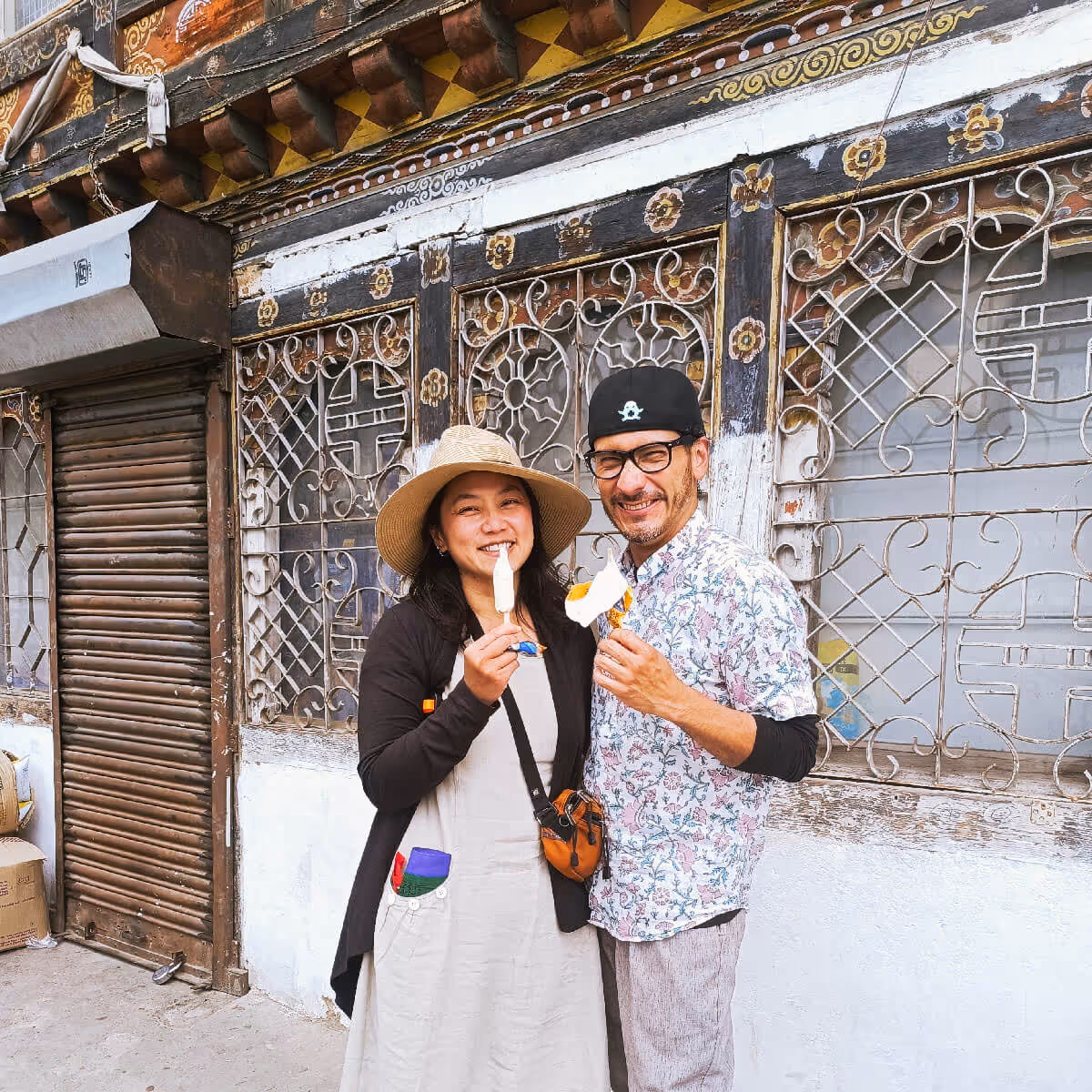 Couple enjoying ice creams together, standing against a rustic Bhutanese shop facade.