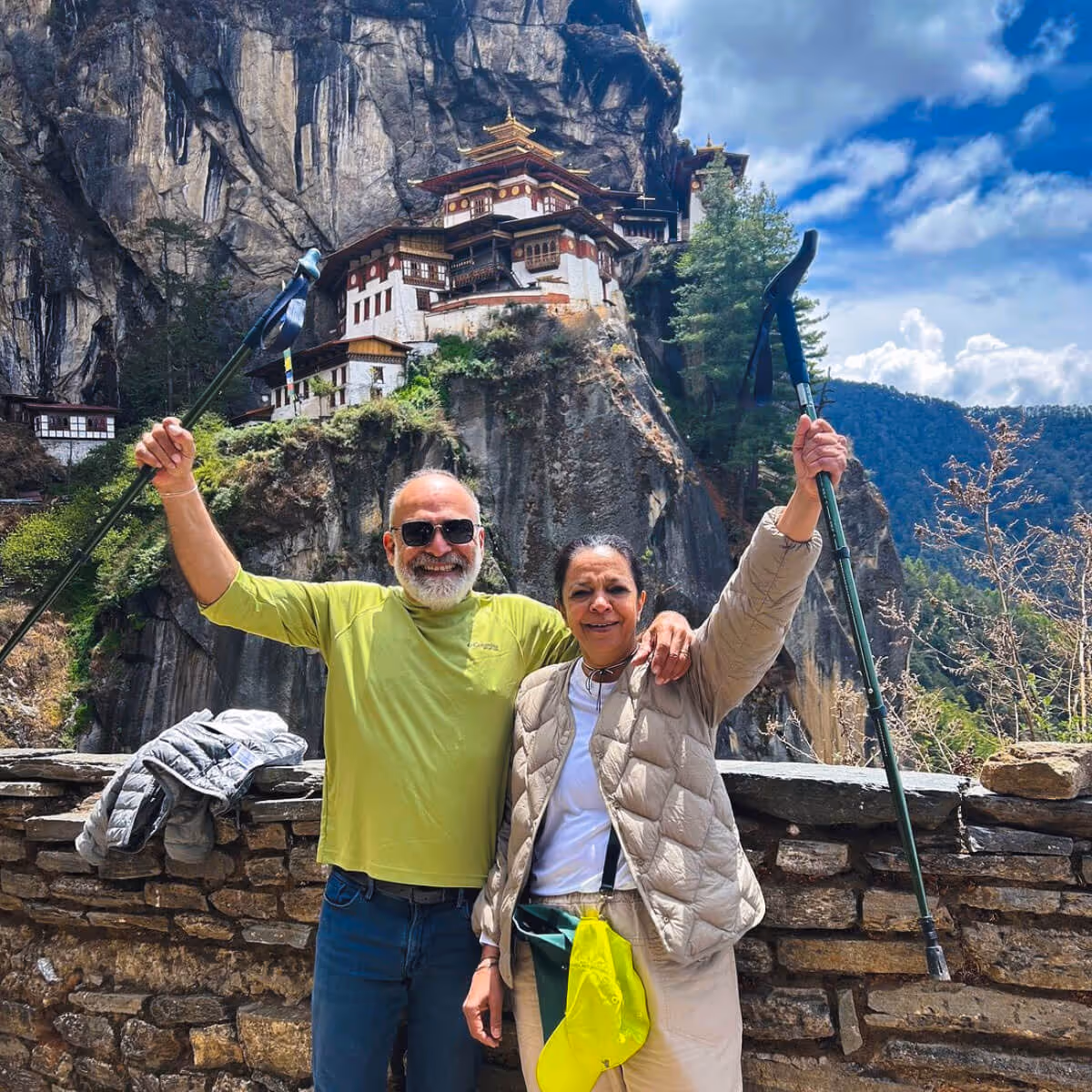 Happy couple posing with trekking poles after their Tiger’s Nest hike, temple dramatically perched on cliff behind.