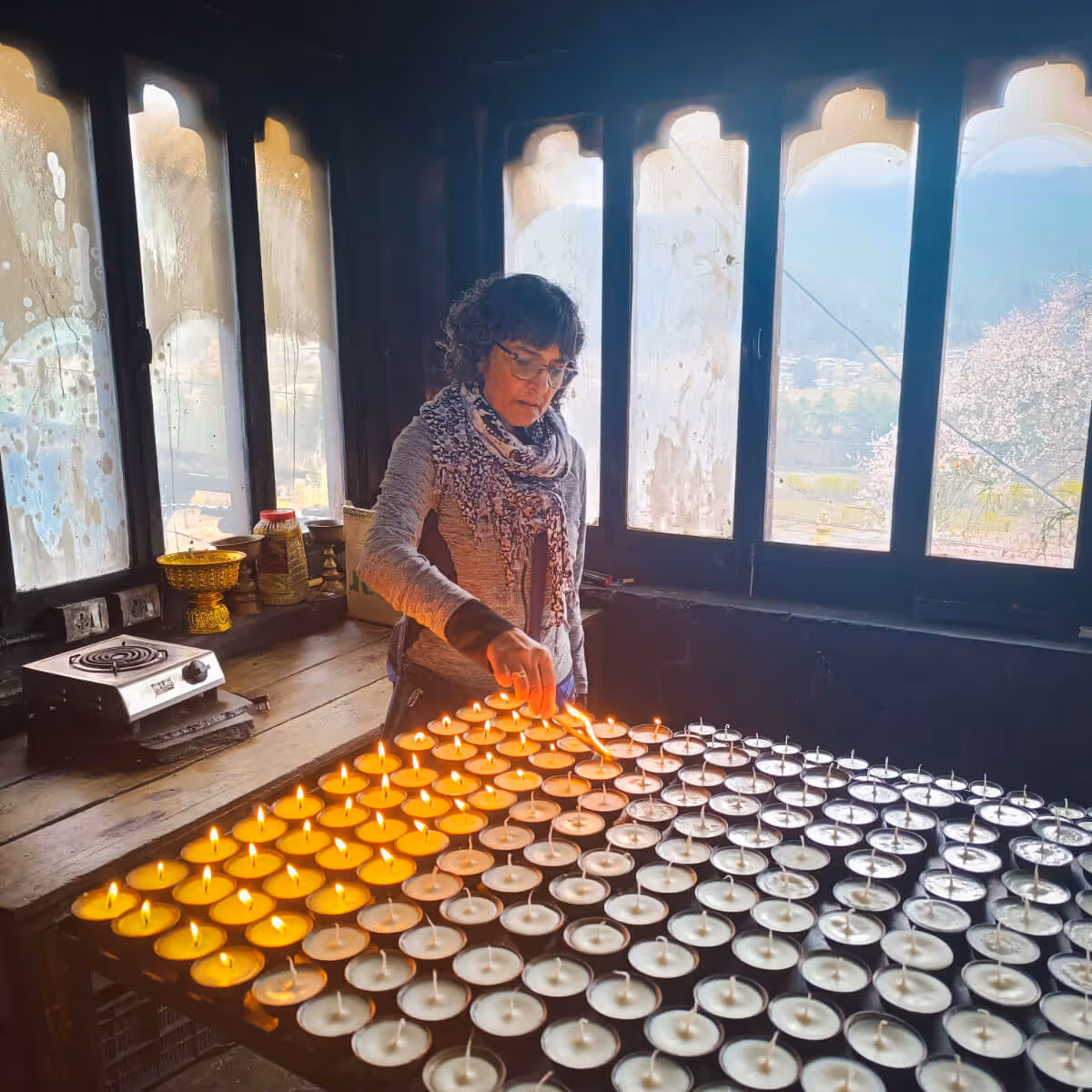 Woman lighting rows of butter lamps inside a dimly lit Bhutanese temple, exuding peace and devotion.
