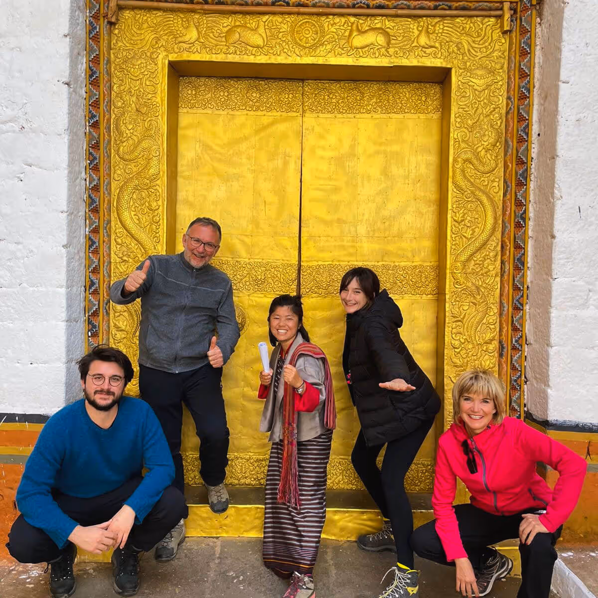 Raven guide and guests joyfully posing in front of a golden temple door in Bhutan.