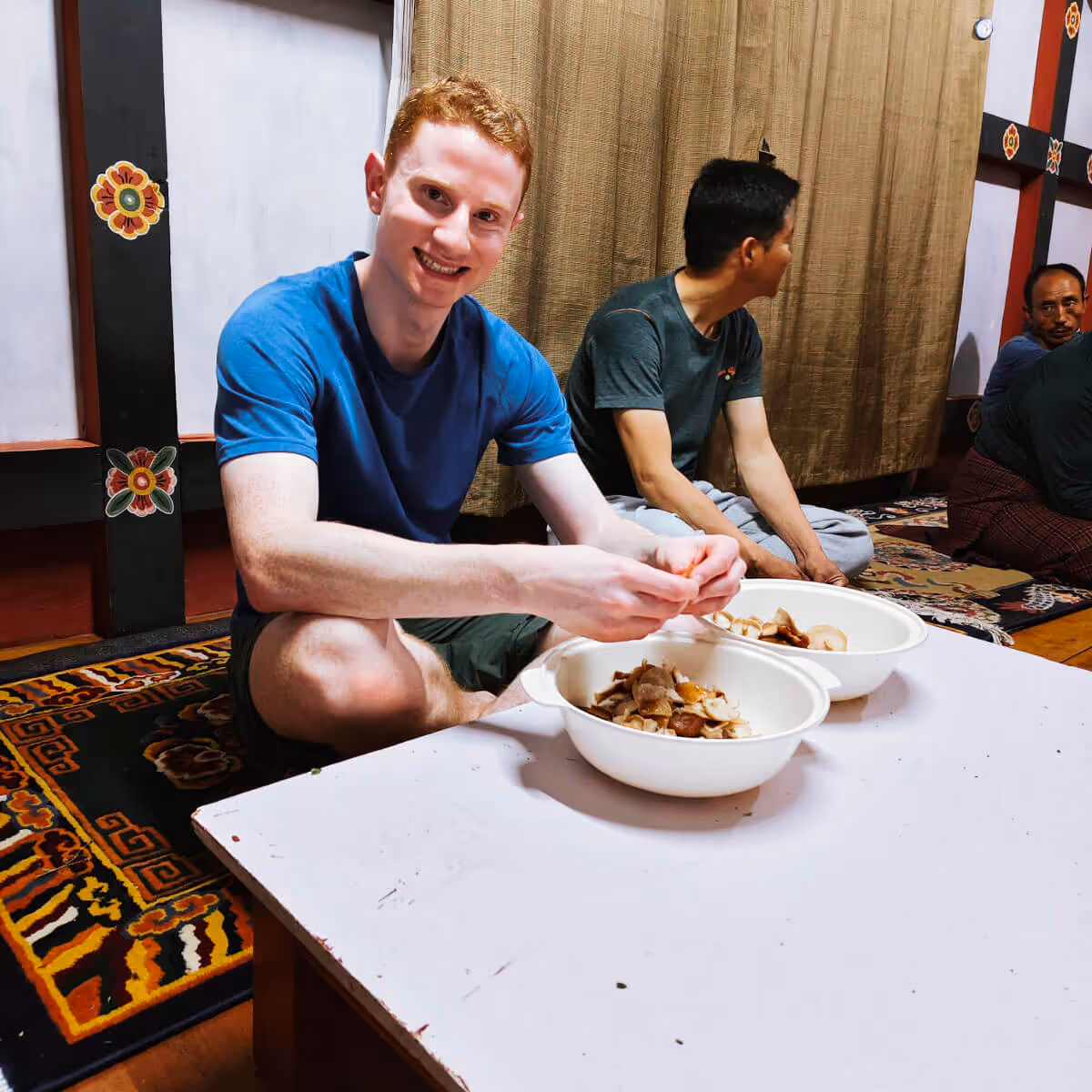 Guest sitting on floor and helping prepare mushrooms during a Bhutanese farmhouse cooking experience.