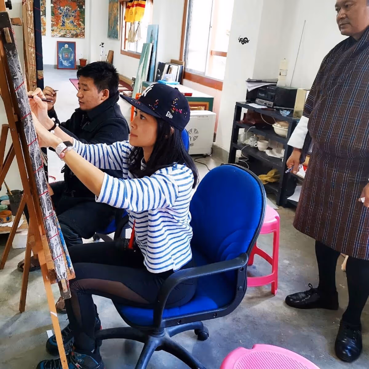 Guest focused on painting traditional art in a Bhutanese studio, guided by local artist.