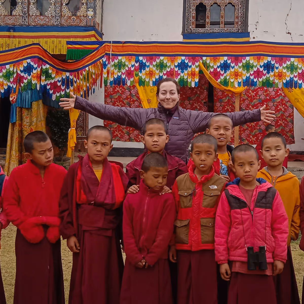 Guest standing happily among young monks in red robes at a monastery courtyard in Bhutan.
