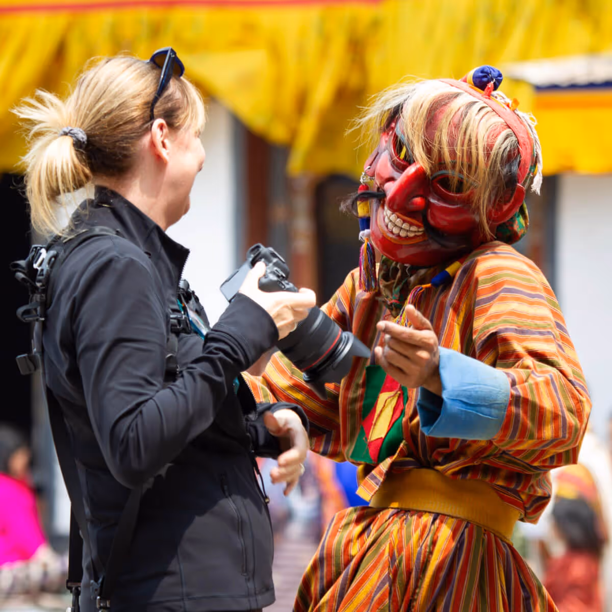 Photographer interacting playfully with a Bhutanese festival clown in colorful costume.