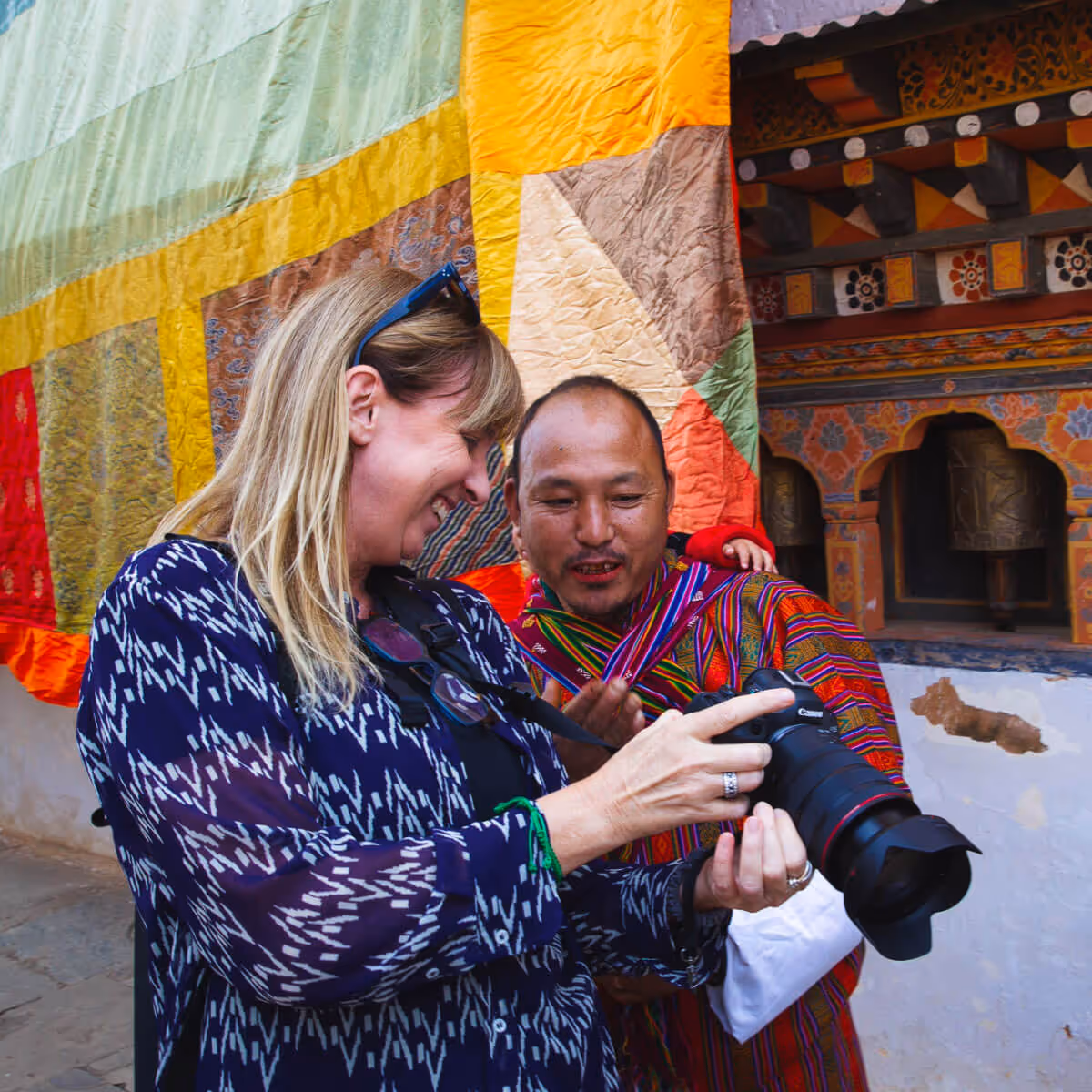Woman sharing camera preview with Bhutanese man in traditional gho at a temple.