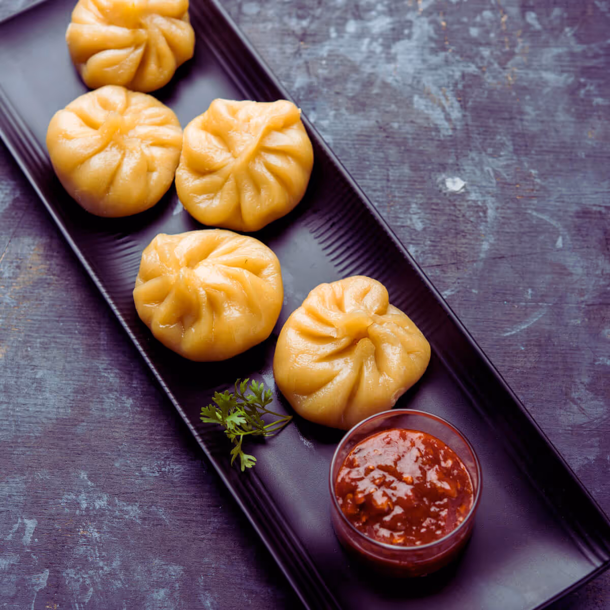 Nepali momos with spicy dipping sauce on a black plate