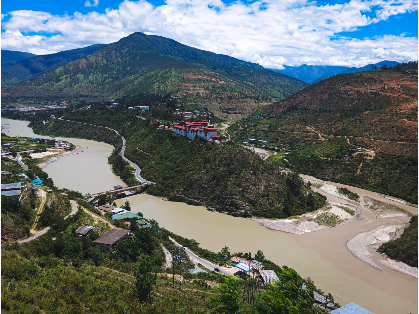 Aerial view overlooking Wangduephodrang Dzong in Bhutan and the rivers below, surrounded by lush green hills.