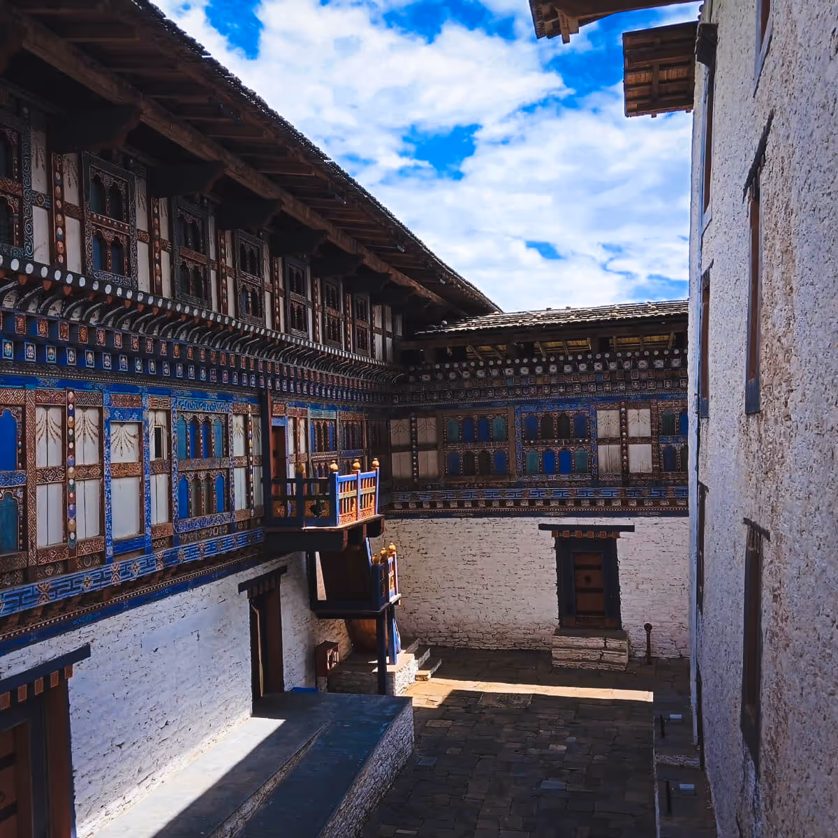 Quiet inner courtyard of Wangdicholing Palace in Bumthang, Bhutan, with ornate painted windows and sunlit whitewashed walls beneath a blue sky.