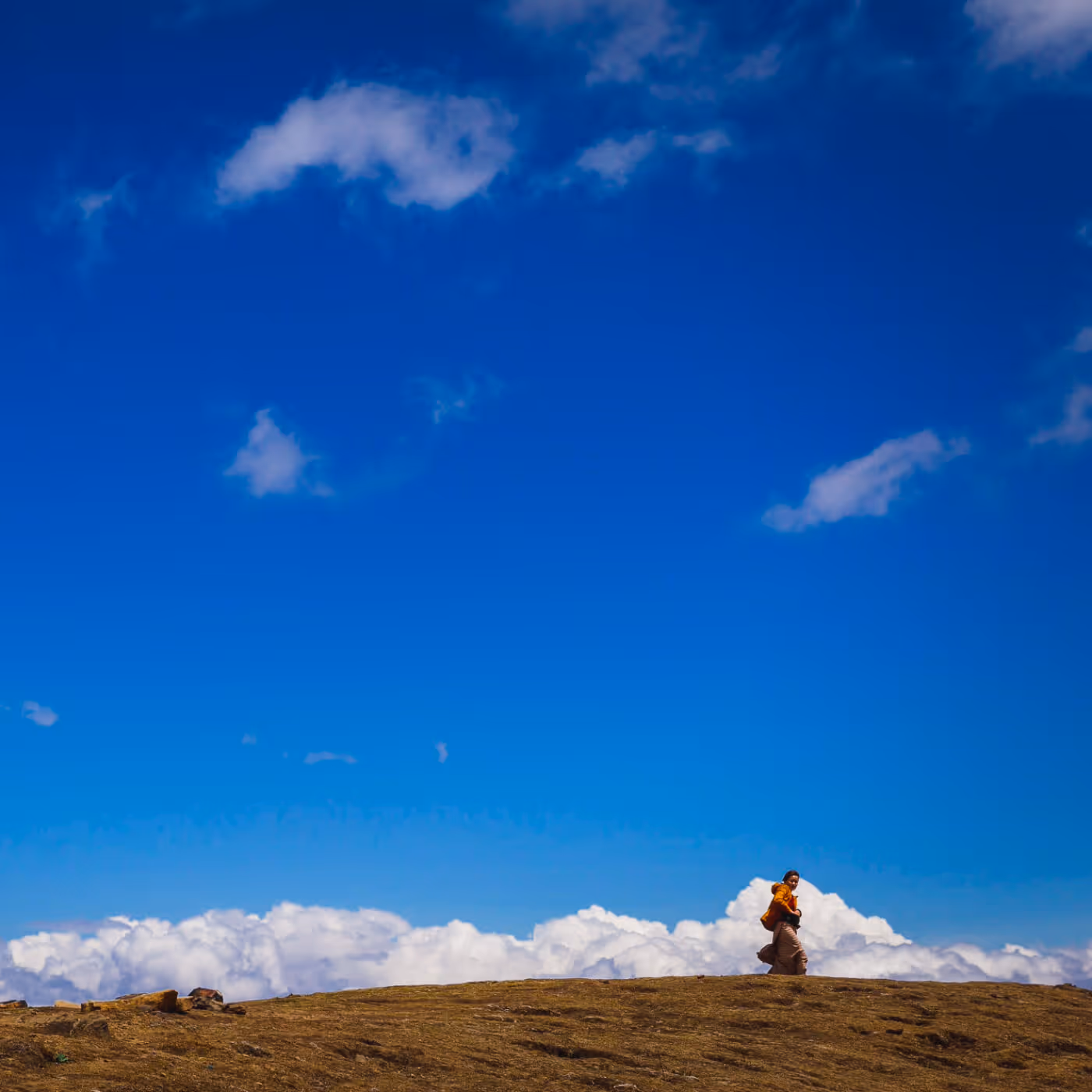A woman in Bhutanese dress walking along a golden ridge beneath a wide, cloud-kissed sky at Chelela Pass.