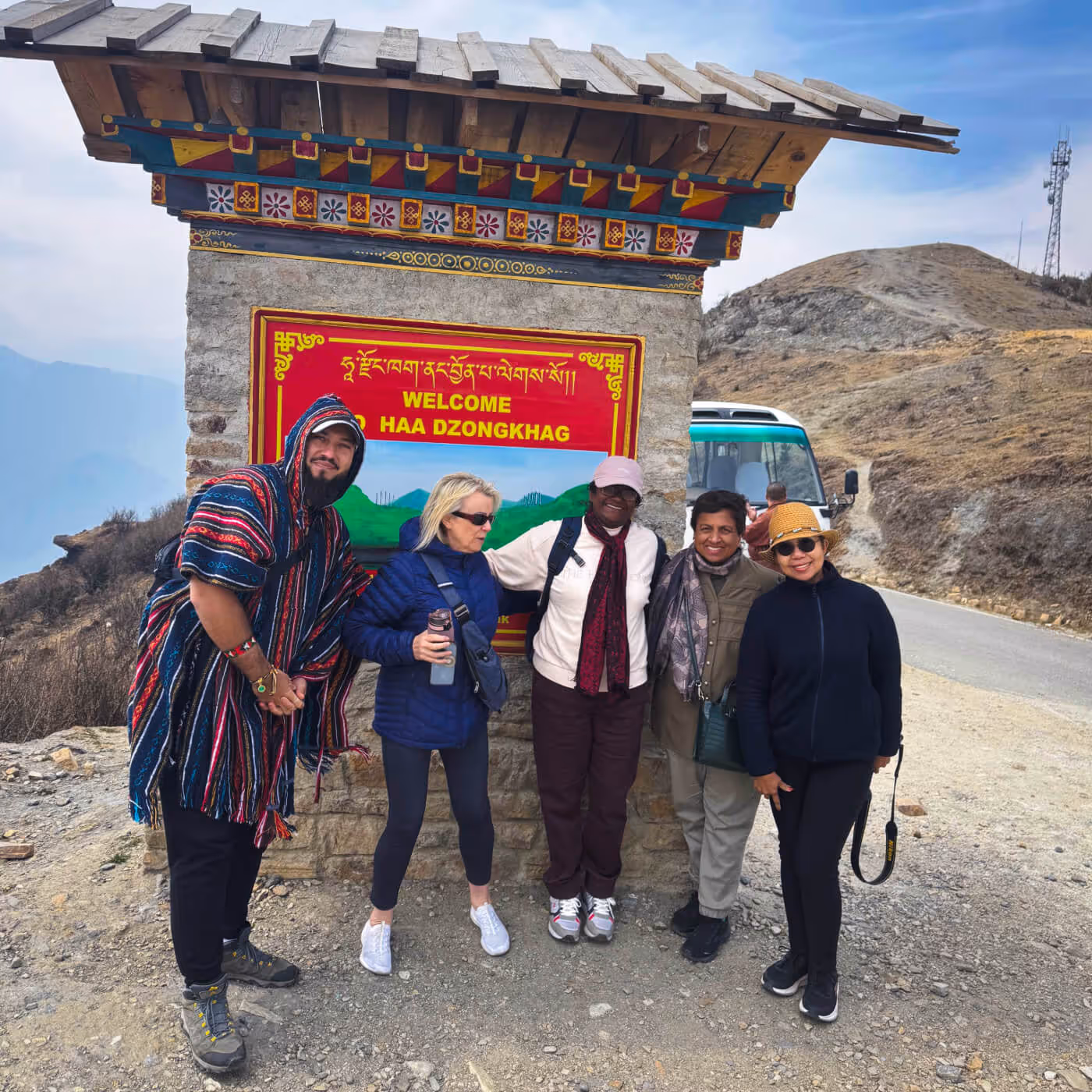 Group of travelers smiling beneath the welcome gate to Haa Dzongkhag after crossing Chelela Pass.