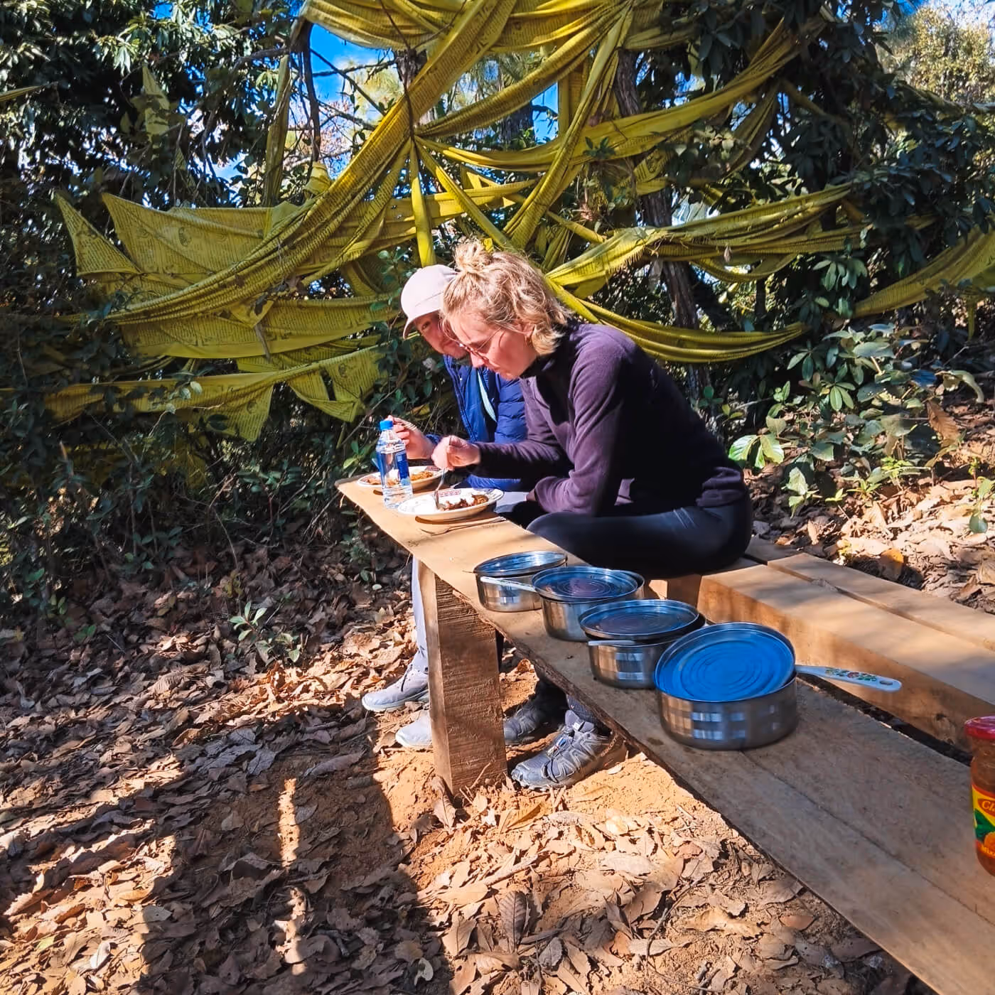 Travelers enjoying a picnic lunch in the woods beside colorful prayer flags