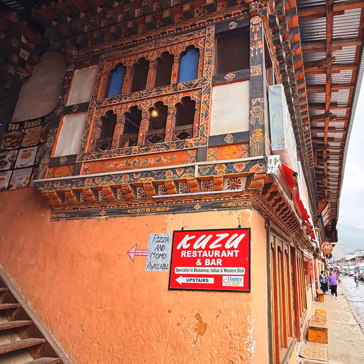 Exterior view of Kuzu Restaurant & Bar in Paro, Bhutan, with its traditional painted windows and welcoming sign inviting guests upstairs.