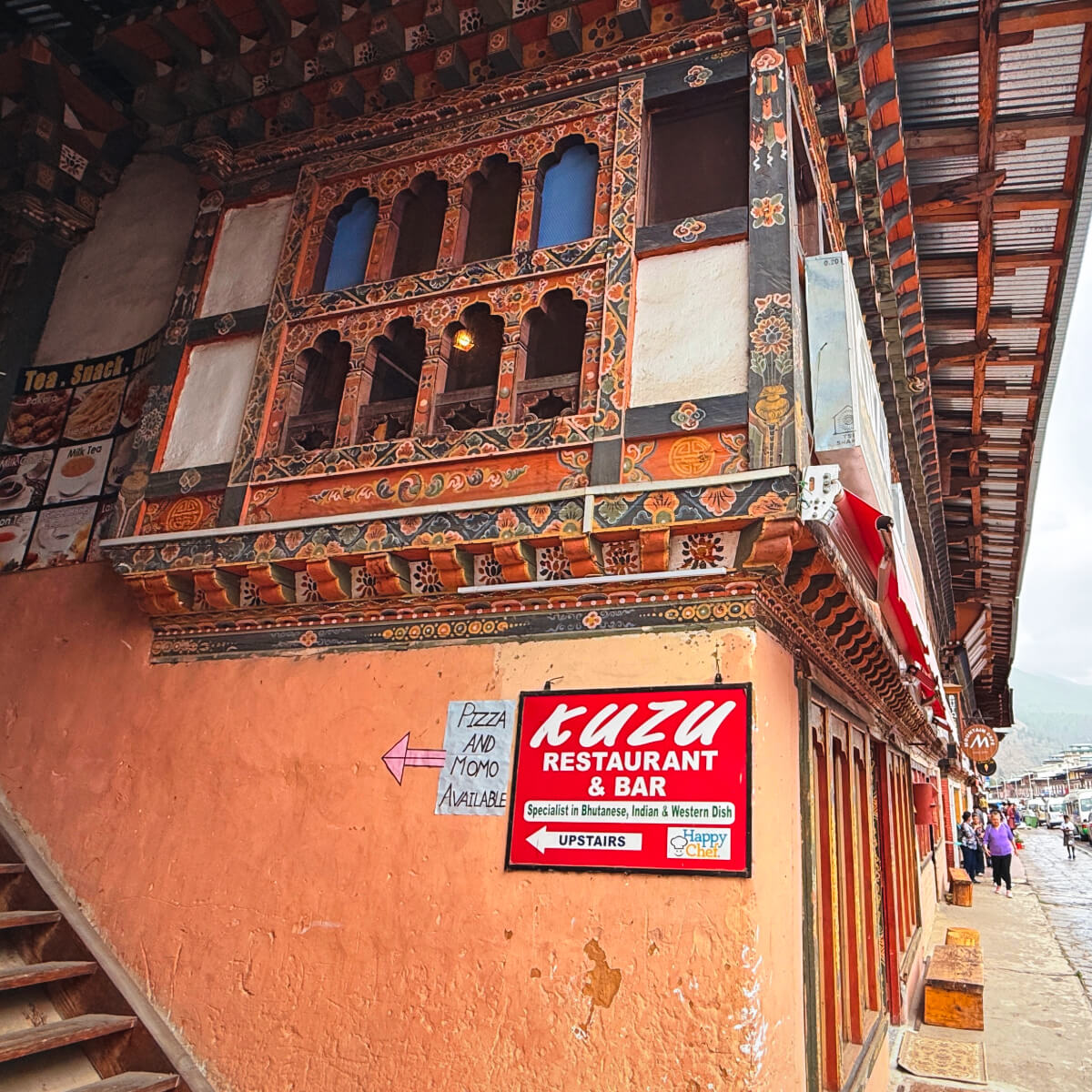 Exterior view of Kuzu Restaurant & Bar in Paro, Bhutan, with its traditional painted windows and welcoming sign inviting guests upstairs.
