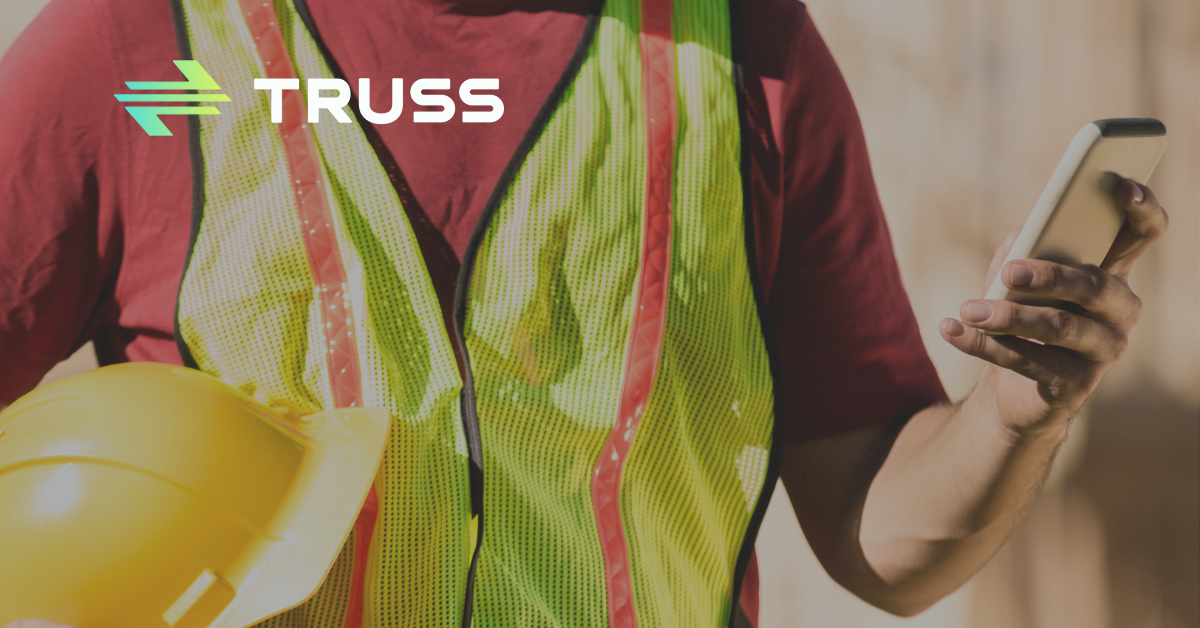 Construction worker using a smartphone while holding a hard hat, symbolizing how SAʴý software helps contractors bring order and control to construction project payments.