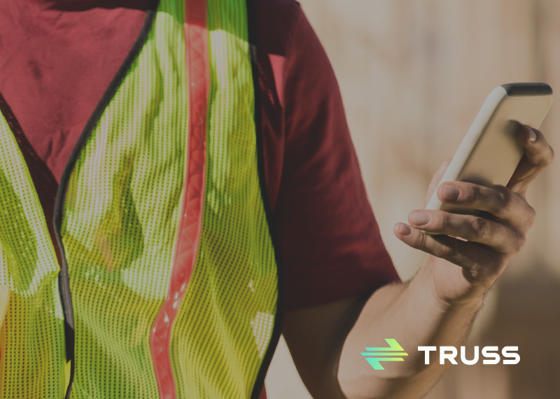 A construction worker in a safety vest checks a smartphone while holding a hard hat, representing how SAʴý helps contractors streamline payments and bring control to construction finances.