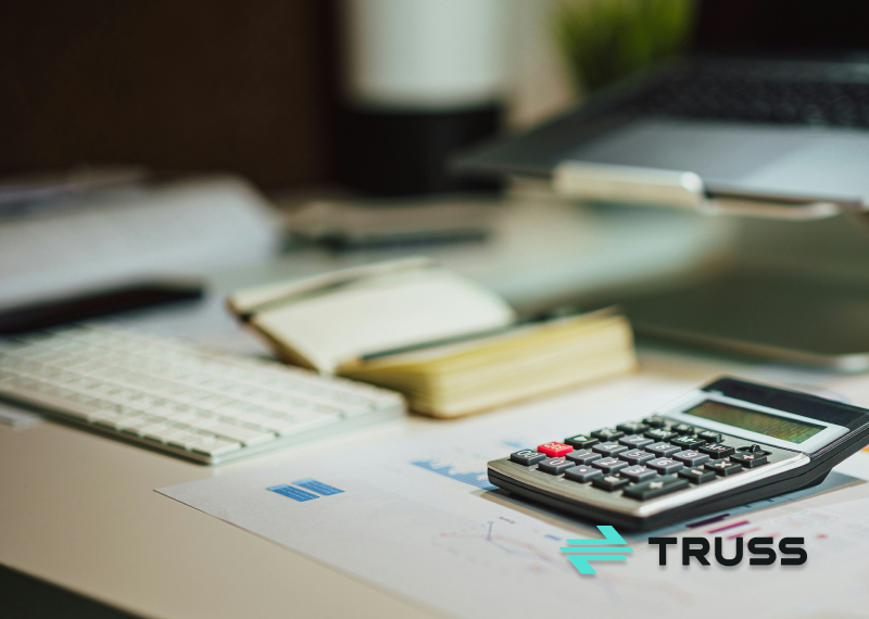 Calculator on financial charts with a laptop and keyboard on a desk, symbolizing how SAʴý helps contractors track construction job costs accurately.