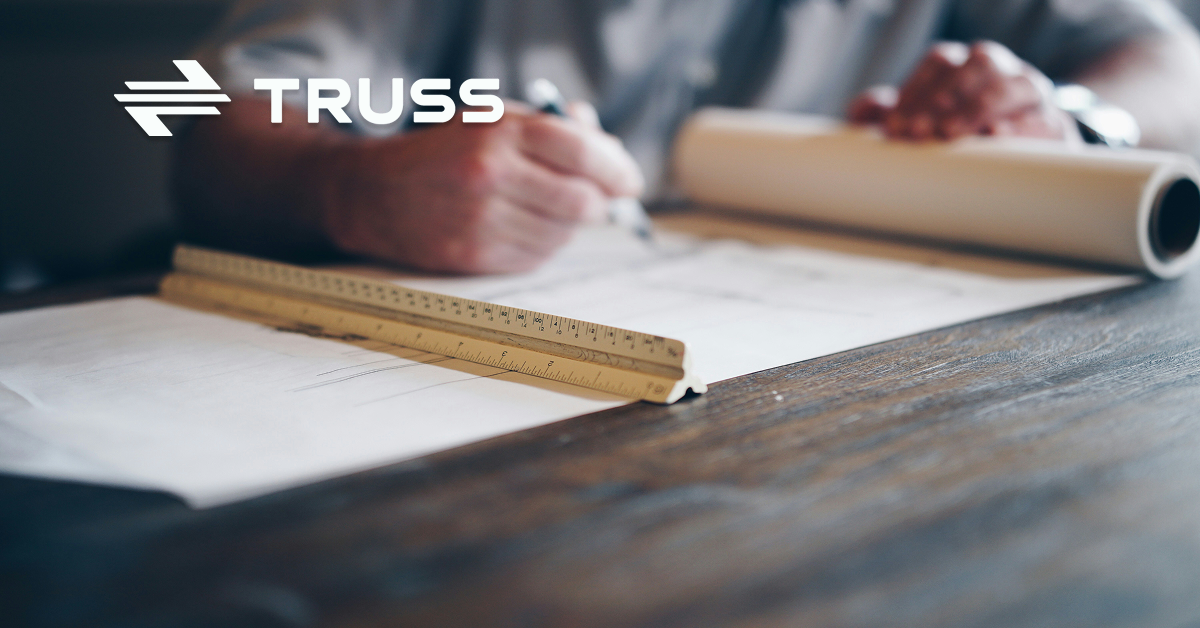 Contractor drafting construction plans on a desk with a ruler and rolled blueprints, representing careful planning and budgeting in construction projects.