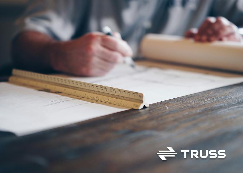 Contractor drafting construction plans on a desk with a ruler and rolled blueprints, representing careful planning and budgeting in construction projects.