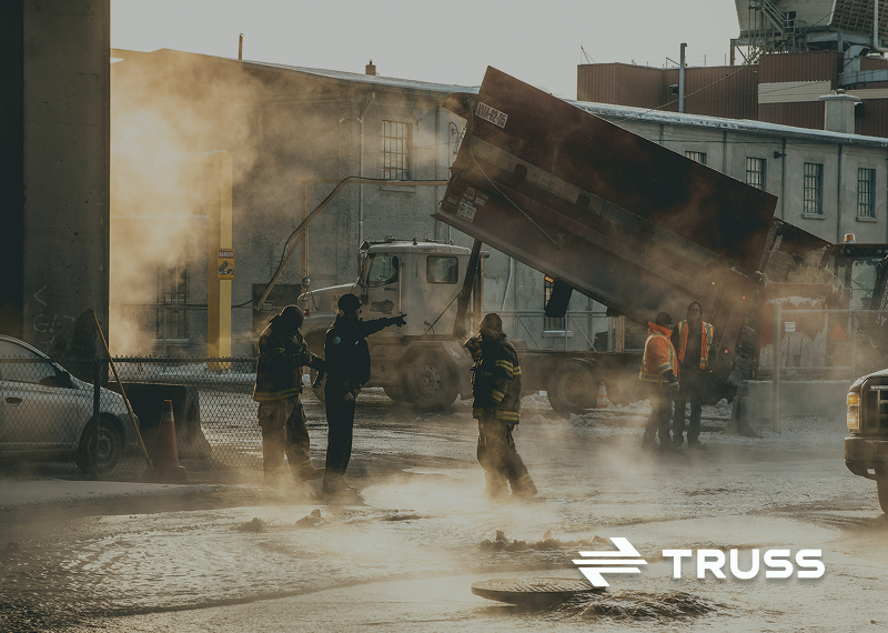 Construction crew working in an industrial site with heavy machinery and steam in the background, representing certified payroll compliance and secure construction payments with Truss.