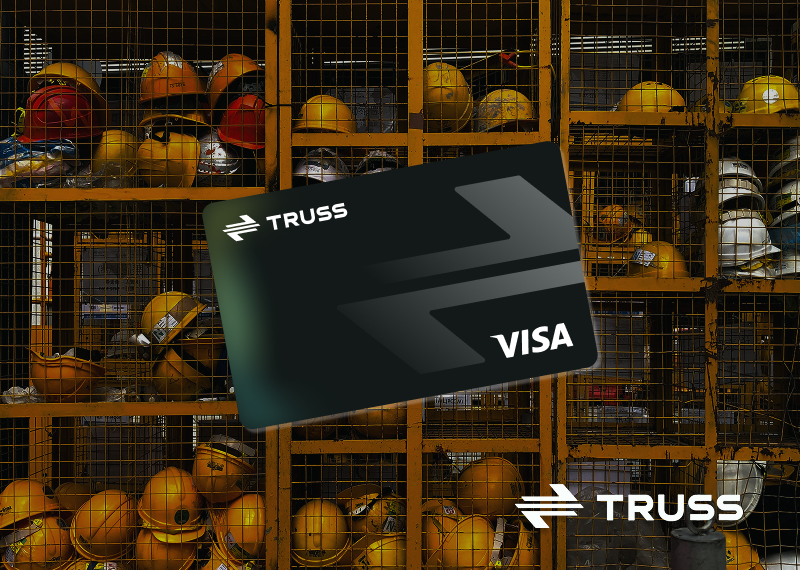 A black Truss Visa business card displayed in front of a construction site locker filled with safety helmets, symbolizing modern financial tools designed for construction businesses.