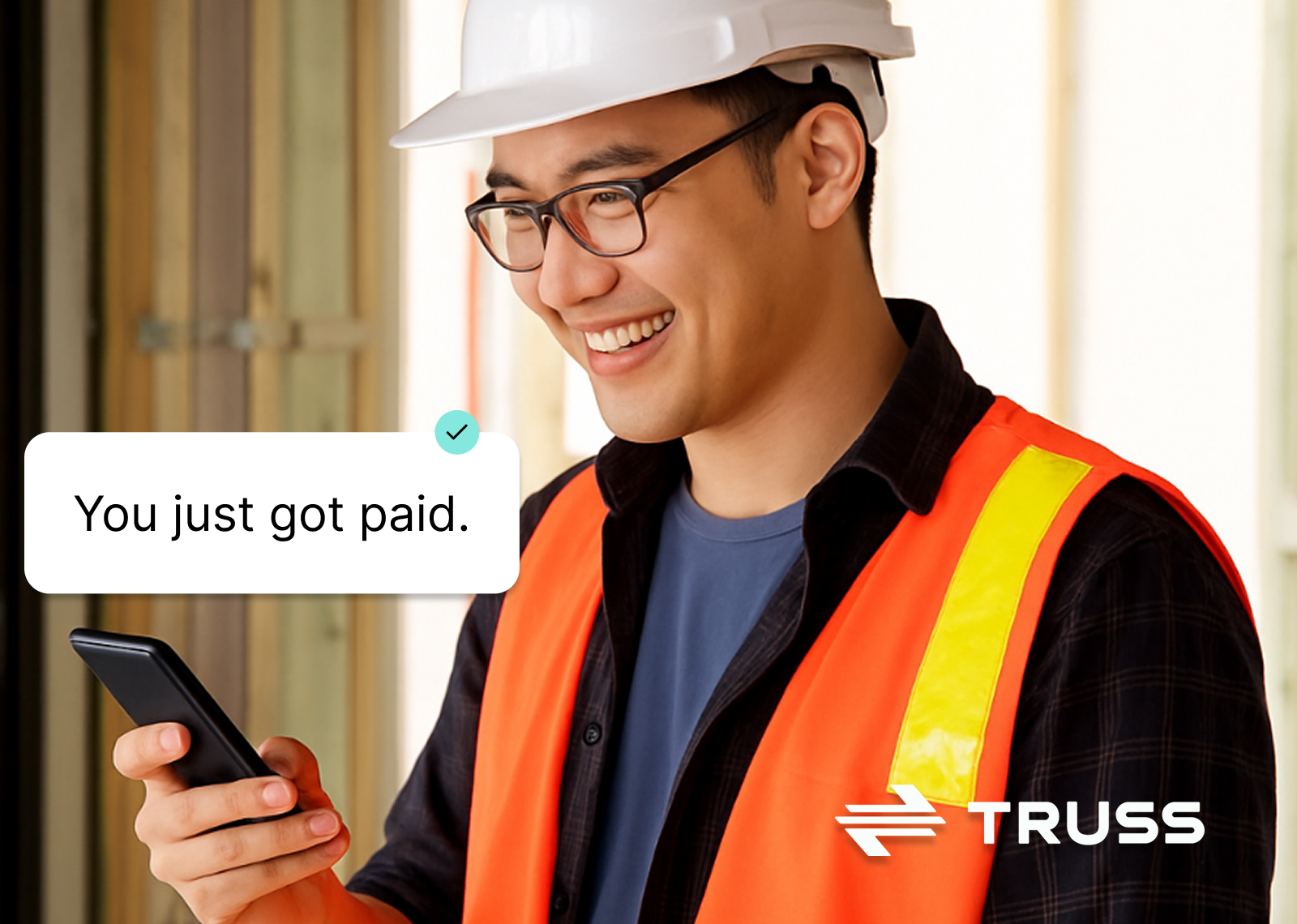 Construction worker smiling while receiving a “You just got paid” notification on his phone, wearing safety gear and standing on a jobsite with the Truss logo above.