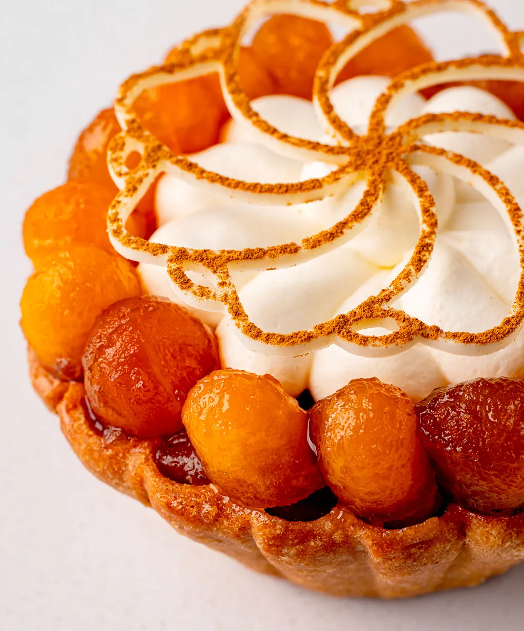 A pastry with a white whipped cream topping and orange slices. Nicolas Rouzaud - Maison de Haute Patisserie creation