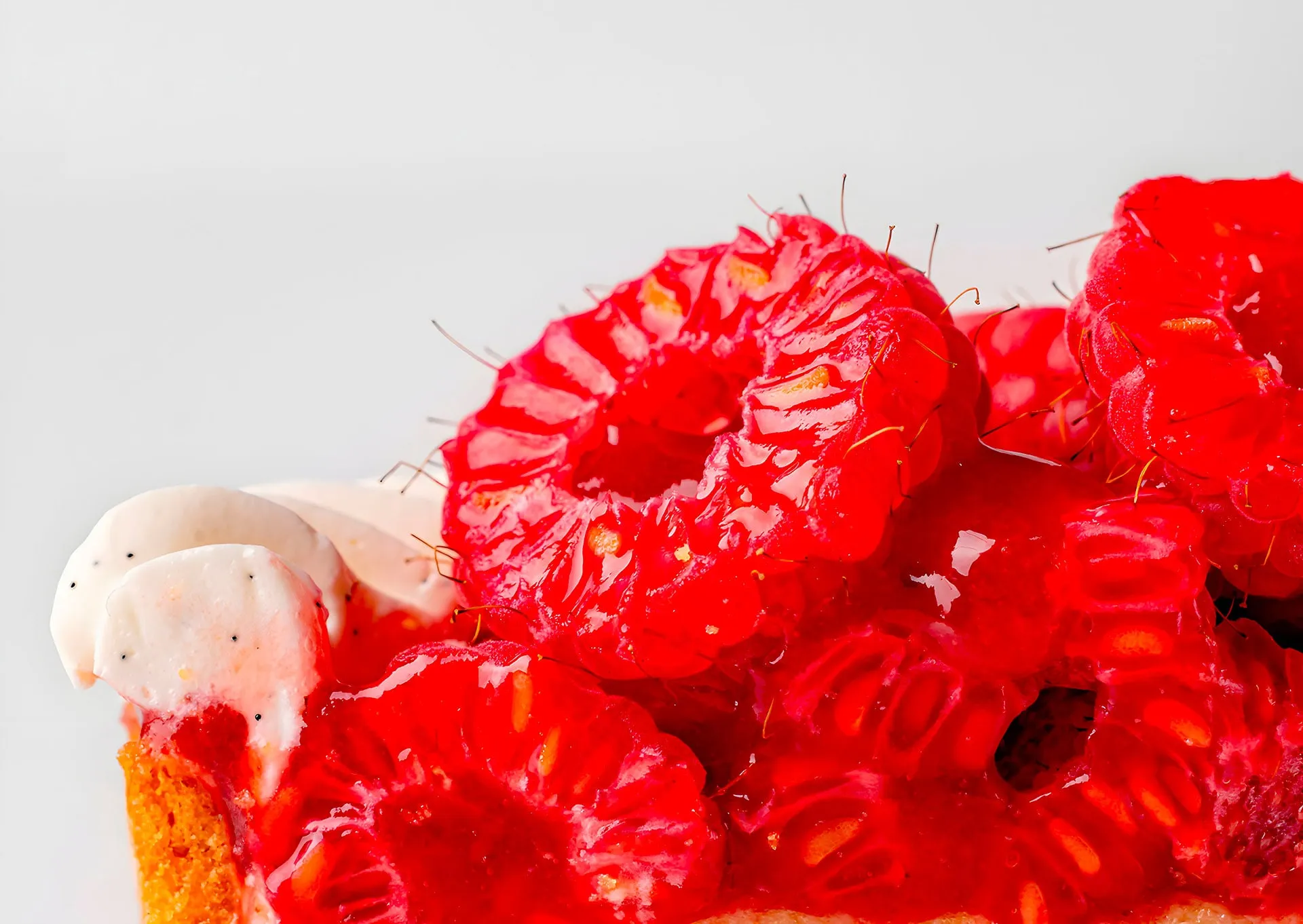 A close-up of a dessert from Maison de Haute Patisserie showcases fresh raspberries glistening with a glossy red glaze, elegantly layered over whipped cream and a soft, golden pastry base. This creation by Nicolas Rouzaud highlights the rich textures and vibrant colors of the fruit.