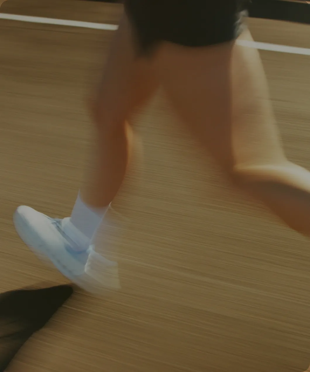 Blurred close-up of a person running on a track wearing white sneakers and white socks.