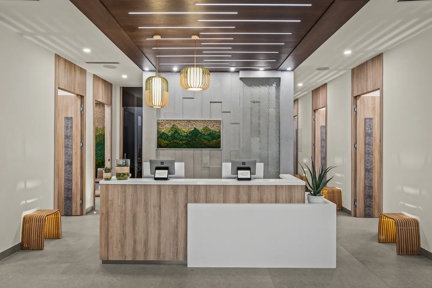 Modern reception area with wooden desk, two computer stations, hanging pendant lights, and numbered wooden doors on either side.