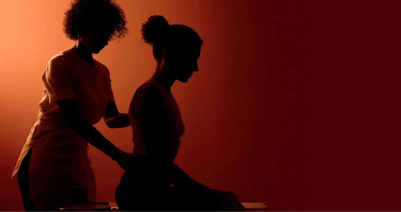 Silhouettes of a person receiving a back massage from another person against a warm orange-red background.