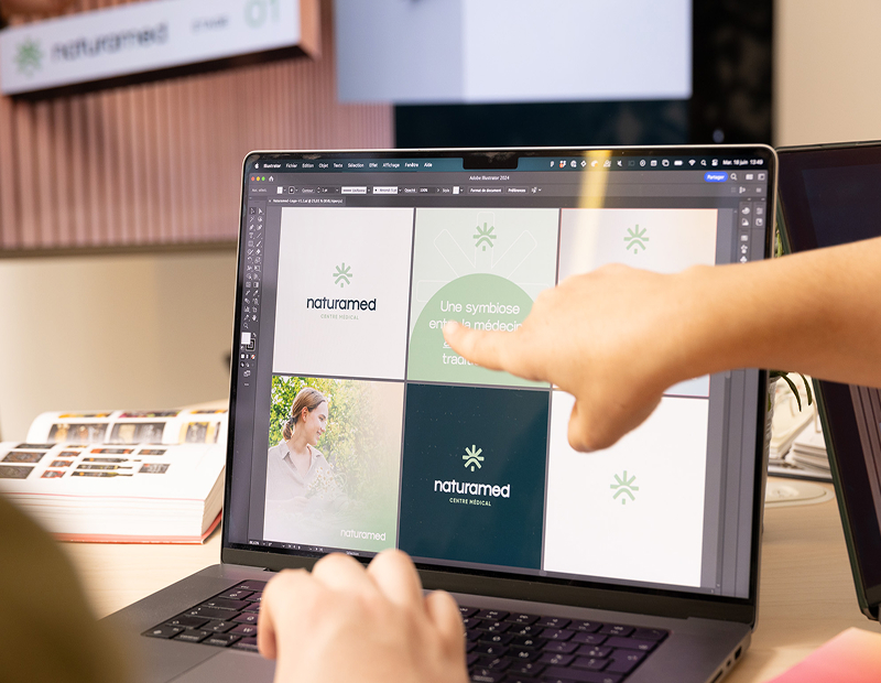Un ordinateur portable affichant un logiciel de design graphique avec le logo et les visuels de Naturamed, une main pointe vers l'écran.
