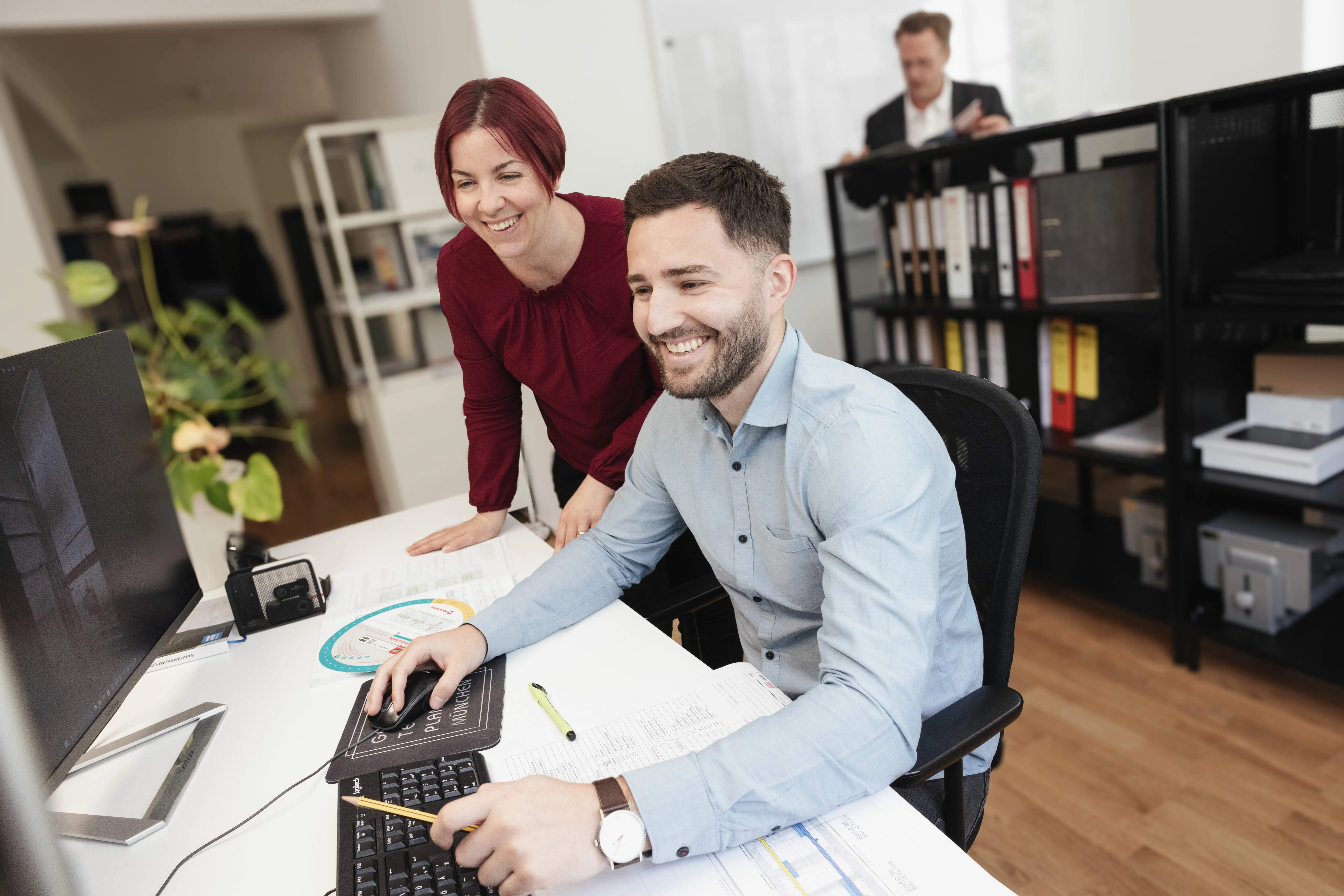 Zwei Kollegen arbeiten gemeinsam an einem Computer in einem modernen Büro.