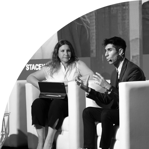 Two people sitting in armchairs engaged in a discussion on stage, one speaking and gesturing.