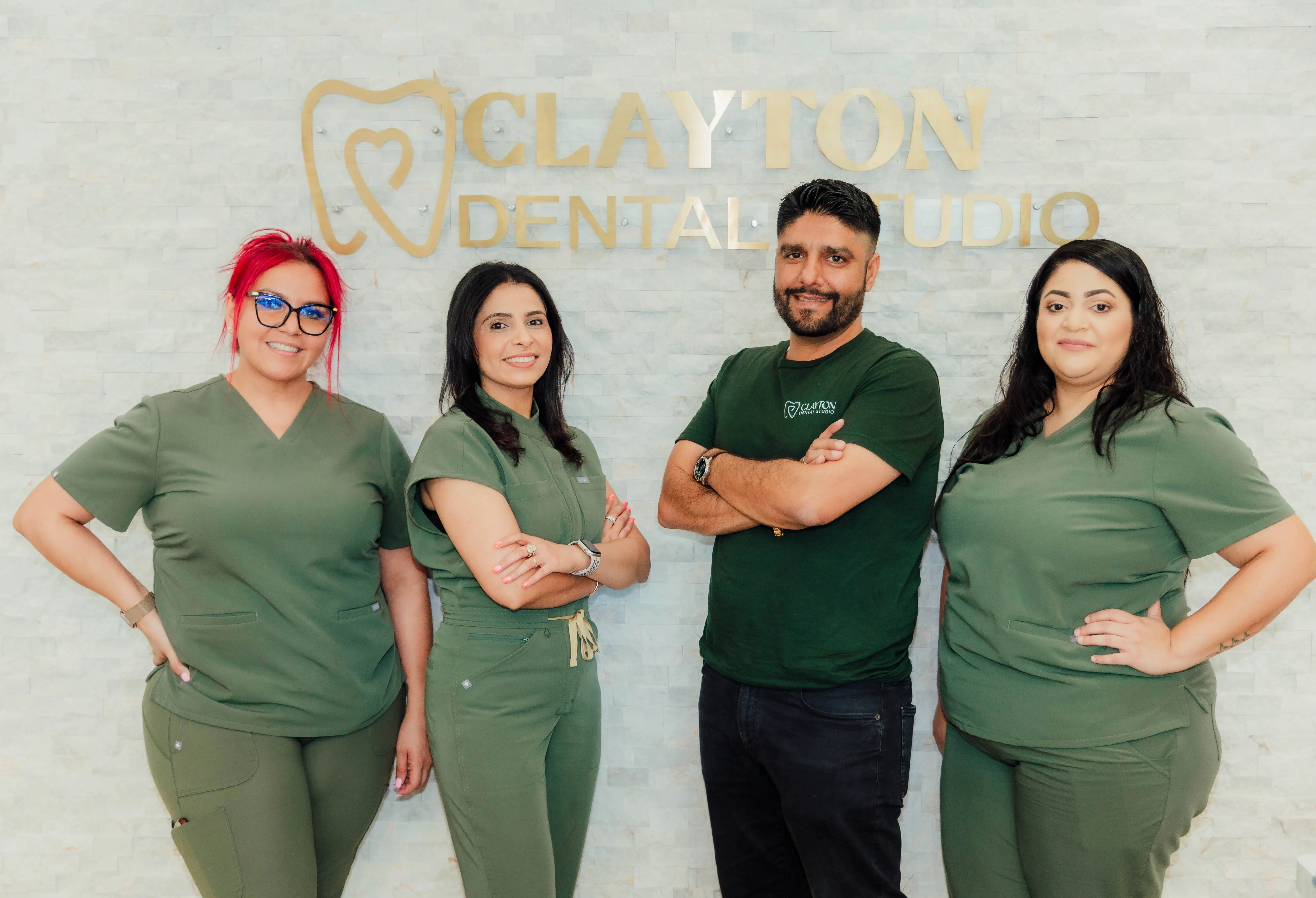 Four dental professionals in green scrubs and a logoed t-shirt standing in front of a Clayton Dental Studio humble, tx sign.