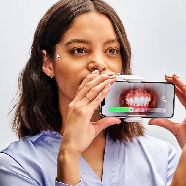 Woman holding a smartphone with a device attached, displaying a close-up image of teeth on the screen.
