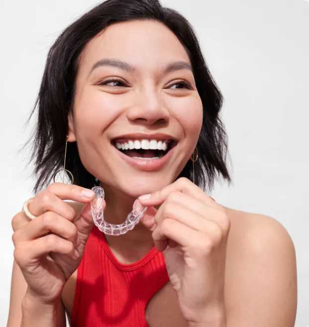 Smiling woman holding a clear dental aligner in front of her mouth.
