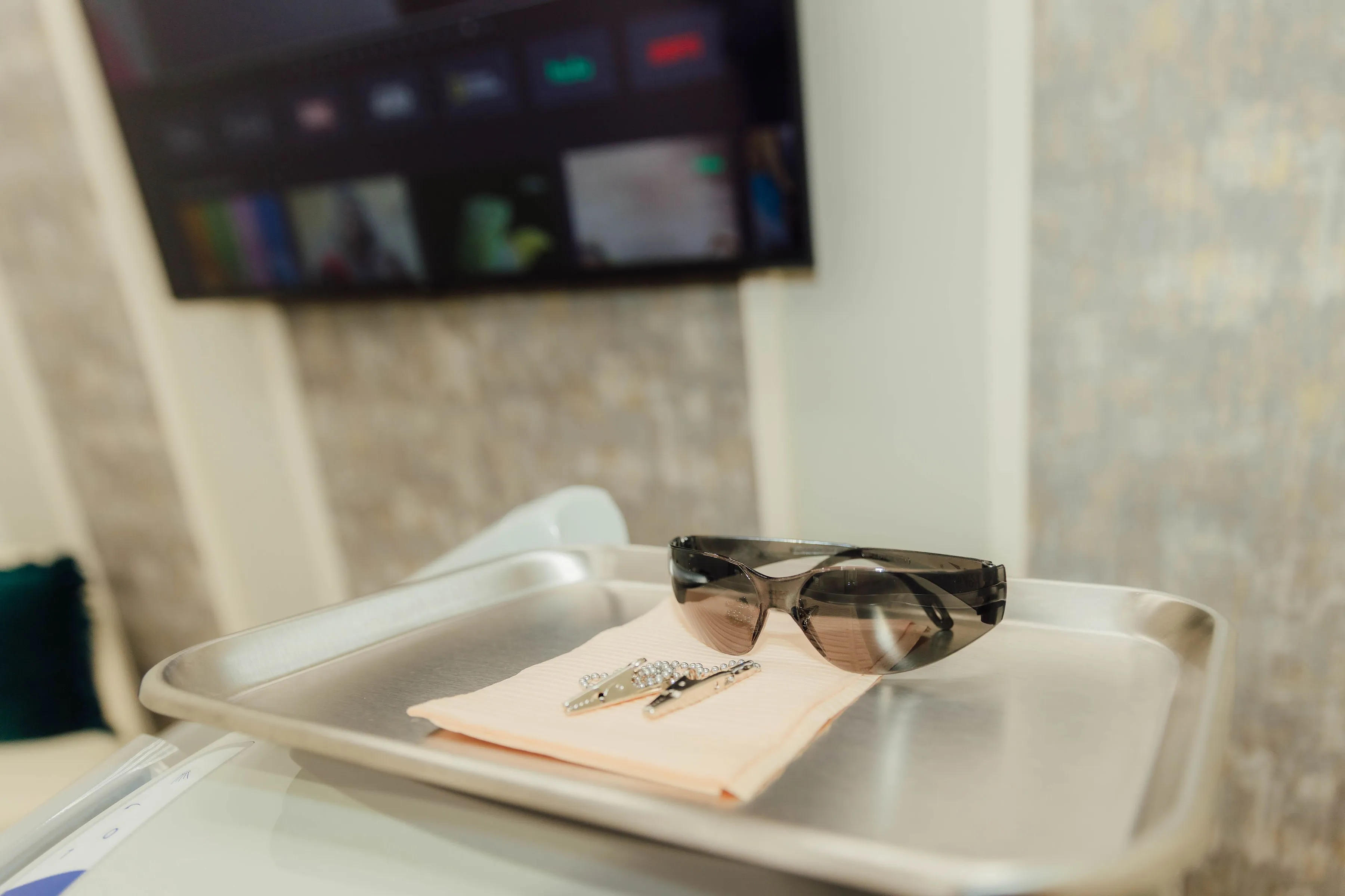Protective tinted eyewear and a metal chain lying on a beige cloth on a metal tray.