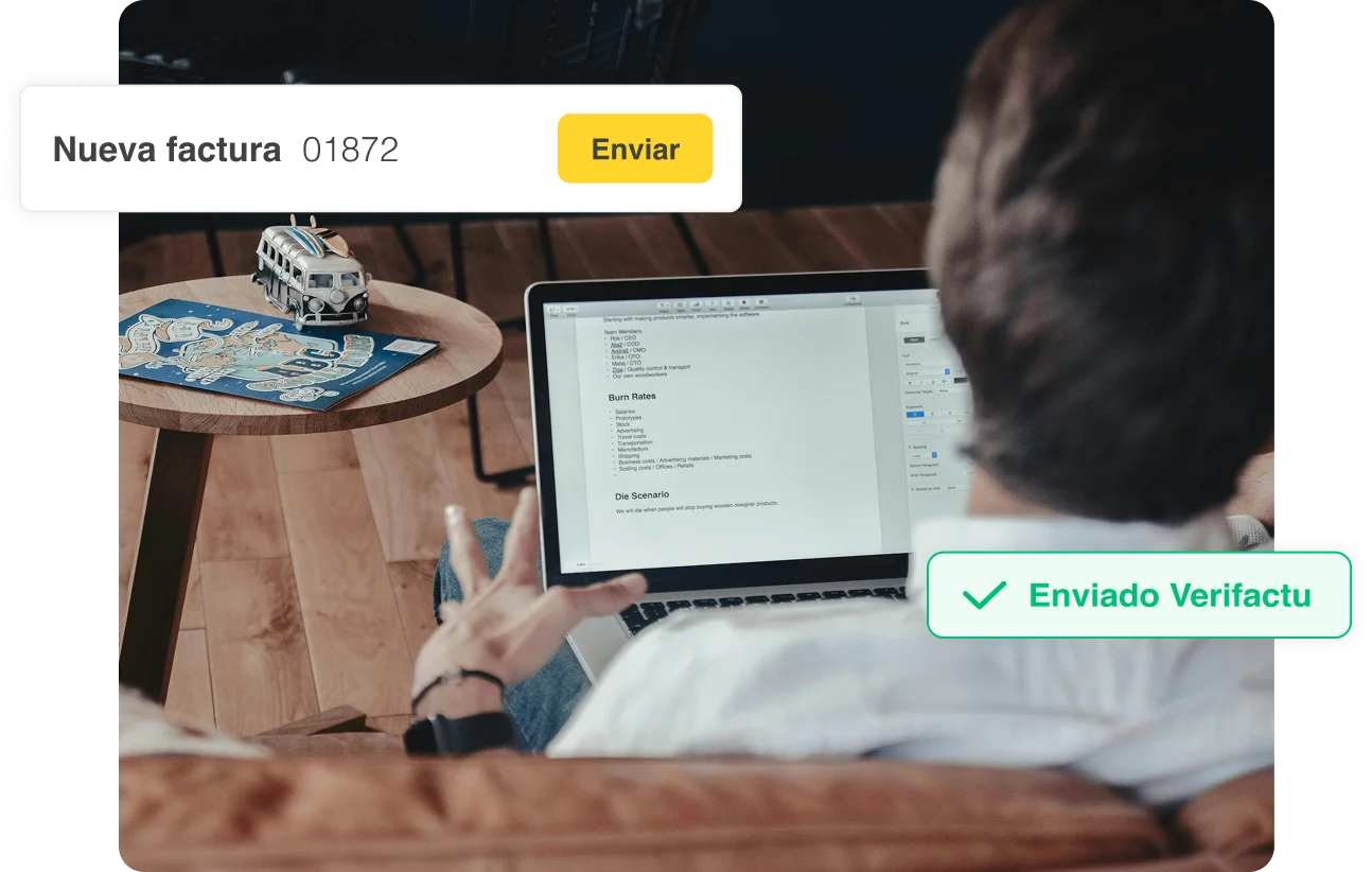 Persona usando una laptop en un sofá con una mesa redonda al lado que tiene un modelo de furgoneta y una revista, mostrando una notificación de factura enviada con éxito.