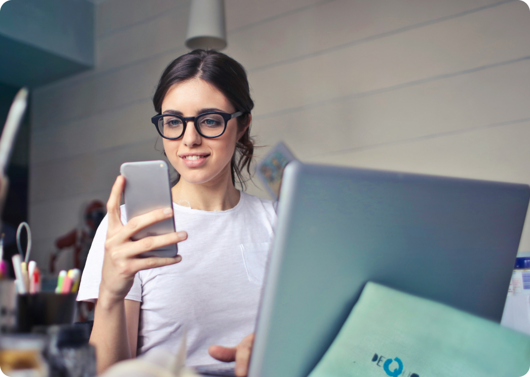 Mujer con gafas usando un teléfono móvil y una computadora portátil, con una interfaz digital que muestra una factura y el logo de Verifactu.
