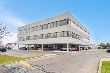 Three-story office building with parking underneath and cars parked around it under a clear blue sky.