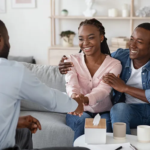 Smiling couple sitting on a couch shaking hands with a man during a counseling session.