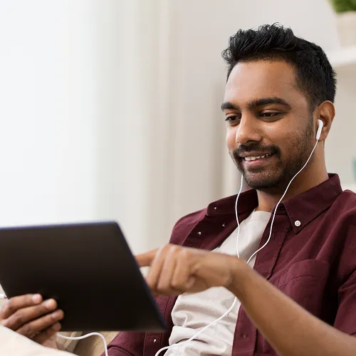Man wearing earbuds using a tablet and smiling indoors.