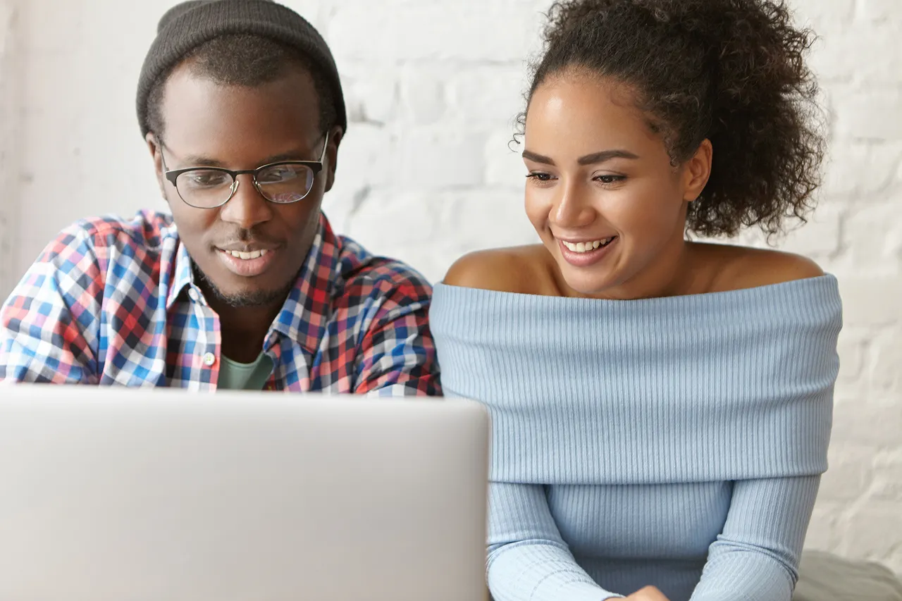 Two young adults looking at a laptop screen, smiling and engaged.