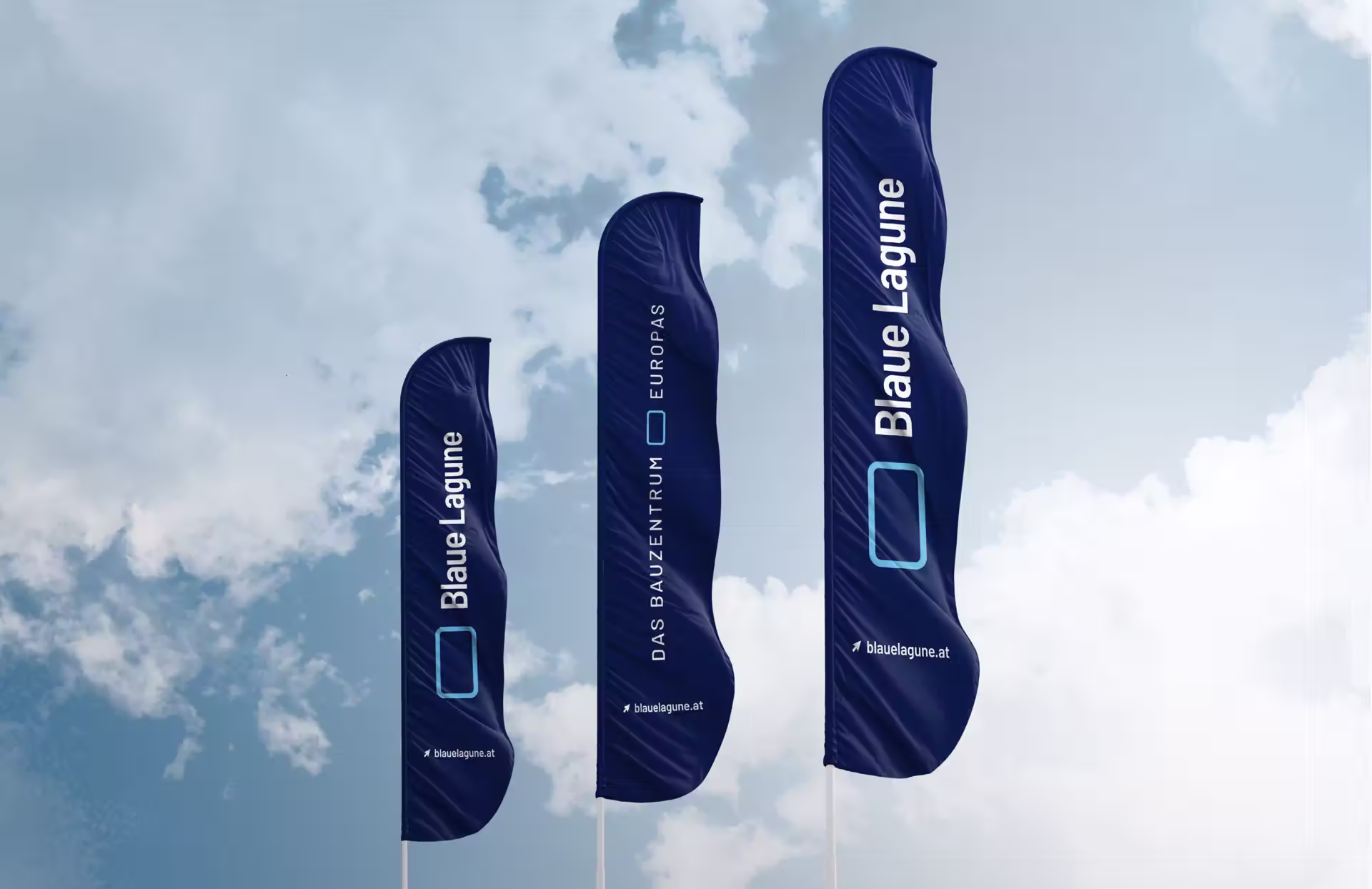Drei dunkelblaue Werbebanner gegen wolkigen Himmel mit „Blaue Lagune“, „Das Bauzentrum Europas“-Text und der Website „blauelagune.at“ mit charakteristischem rechteckigem Logo-Element