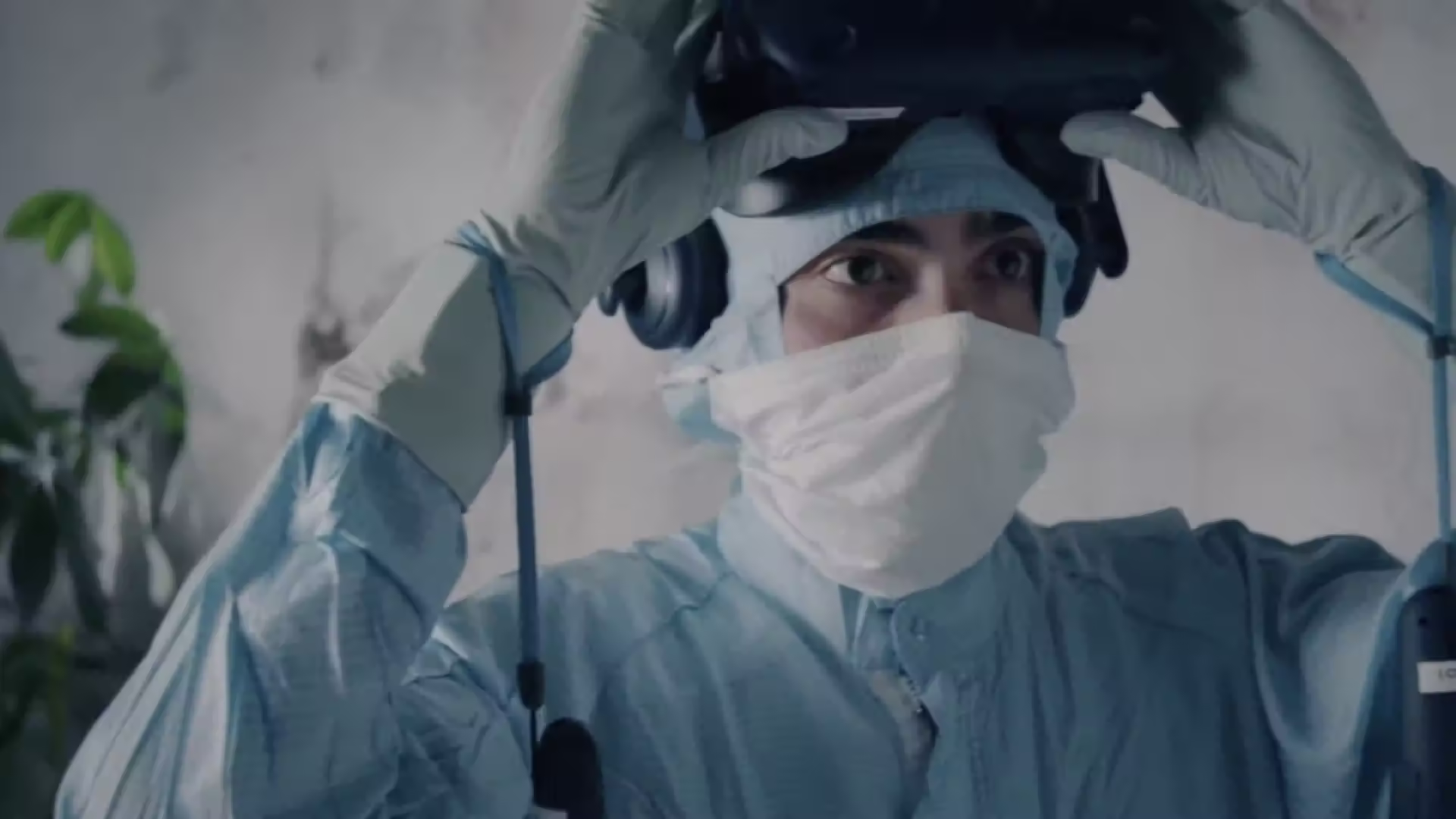 Person in vollständiger Schutzkleidung mit Gesichtsmaske und Schutzbrille arbeitet in steriler pharmazeutischer Produktionsumgebung